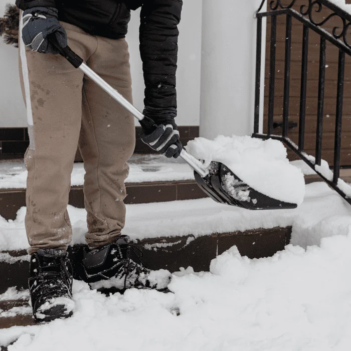 Mitarbeiter schaufelt Schnee auf einer Treppe